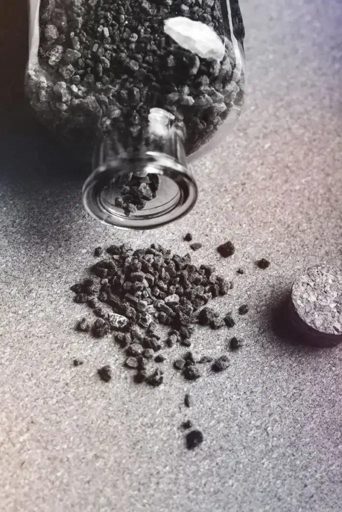 From above black and white of activated carbon granules scattered on table from glass jar with cork