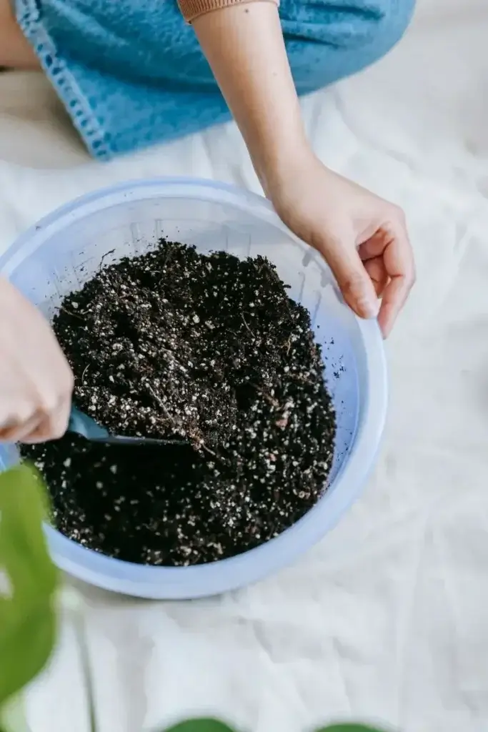 From above of crop anonymous female gardener sitting on floor with shovel and digging soil in pot for home plant