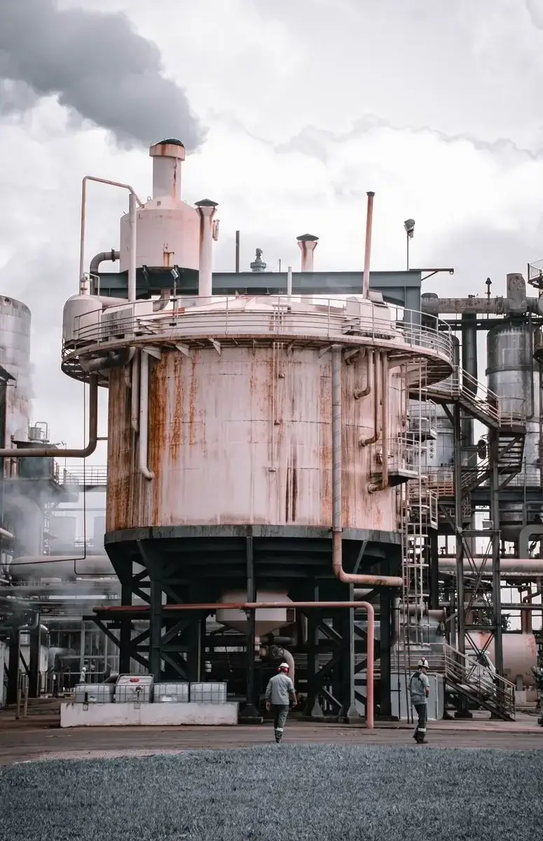 Rusty industrial tank emitting smoke with workers on site, showcasing pollution and industry.