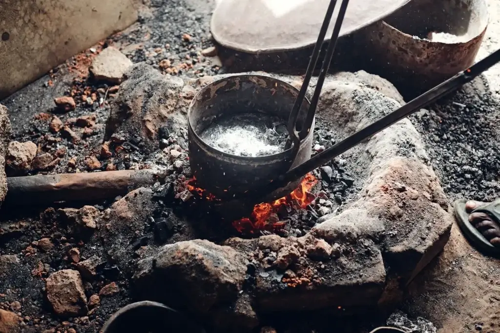 Close-up of an iron pot heating over open fire in a traditional metal forging process.
