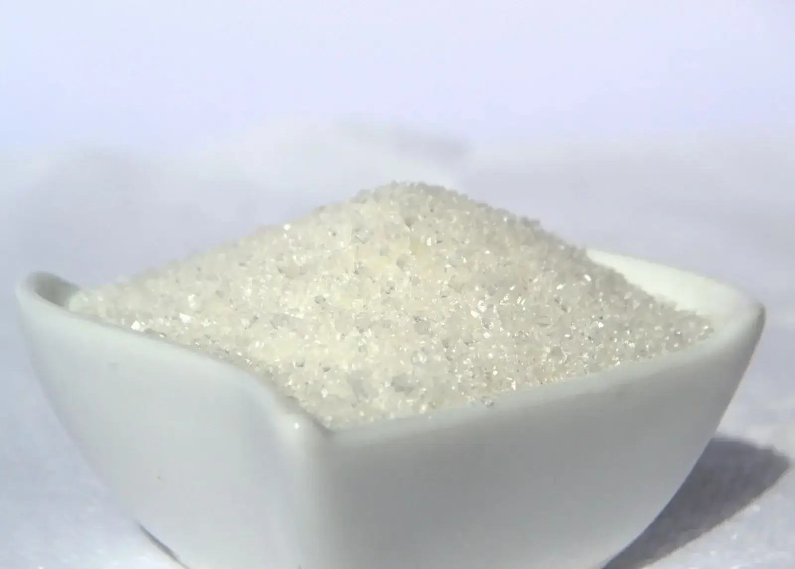 Eine Makroaufnahme, die die Struktur grober weißer Zuckerkristalle in einer weißen Schüssel zeigt.