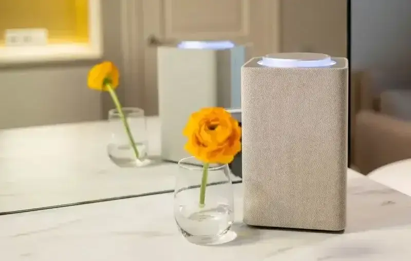 Stylish interior featuring a speaker and an orange flower in a glass vase on a marble surface.