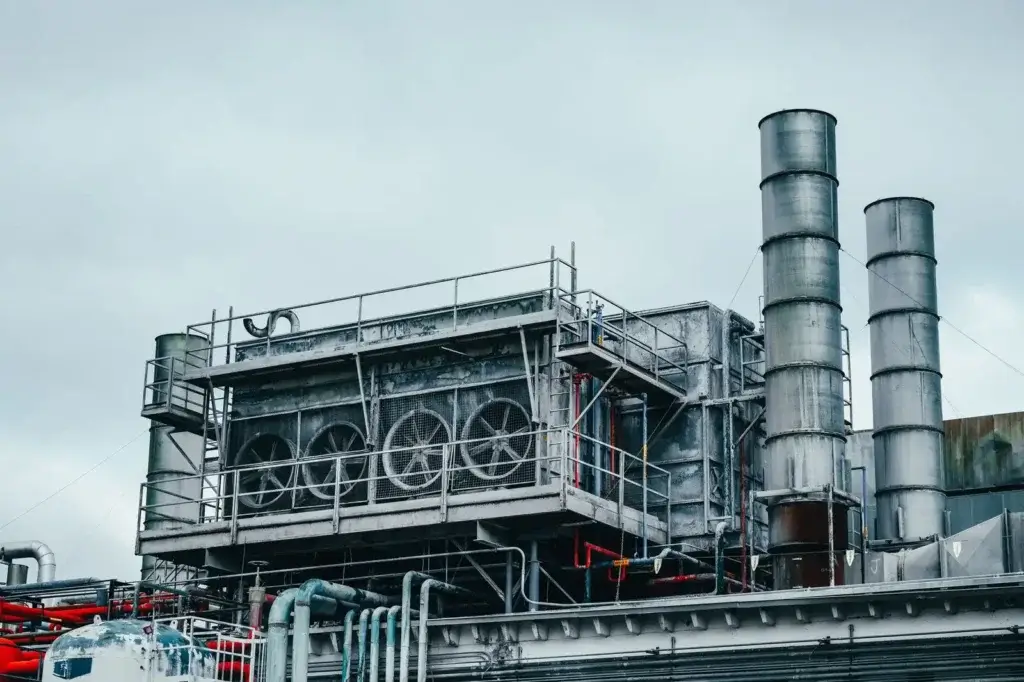 흐린 날 낮 시간대, 공장에 위치한 금속 튜브가 설치된 대형 산업 시설의 외부 전경