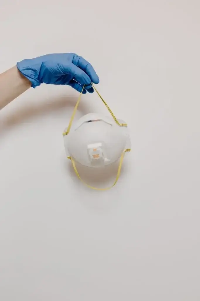 Eine Hand mit Handschuh, die eine N95-Maske vor einem schlichten Hintergrund hält, um wichtige Bestandteile der Schutzausrüstung zu veranschaulichen.